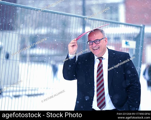 04 December 2023, Hamburg: Ties Rabe (SPD), Senator for Schools and Vocational Training in Hamburg, protects himself from the snowfall with a file folder in the...