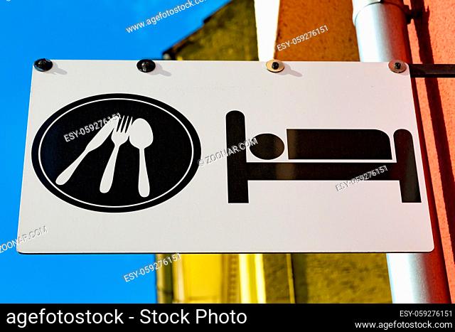 Sign for sleeping accommodation and restaurant on a pole outside a colorful yellow and orange building