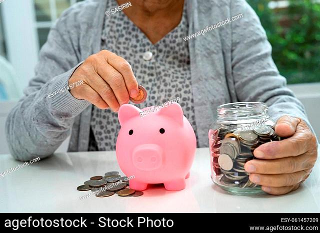 Asian senior or elderly old lady woman holding counting coin money in piggy bank. Poverty, saving problem in retirement