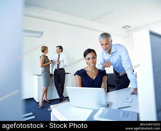 Mature businessman and businesswoman using laptop with colleagues discussing in office