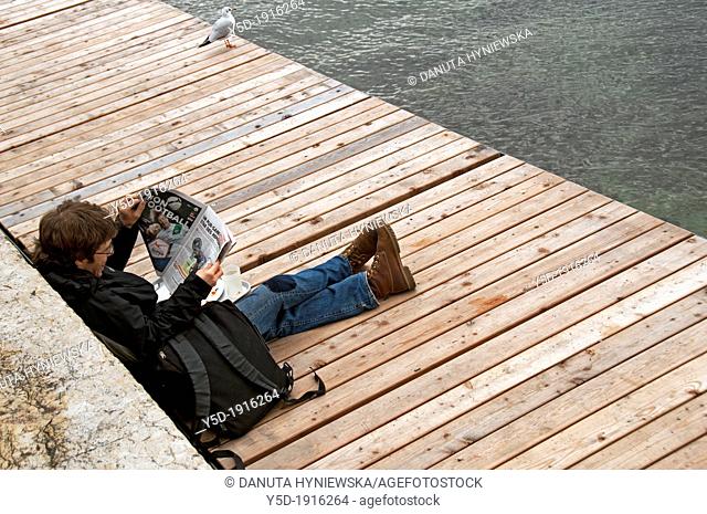 single man resting, sitting next to water reading newspapr, Paquis beach, autumn time, Geneva, Switzerland