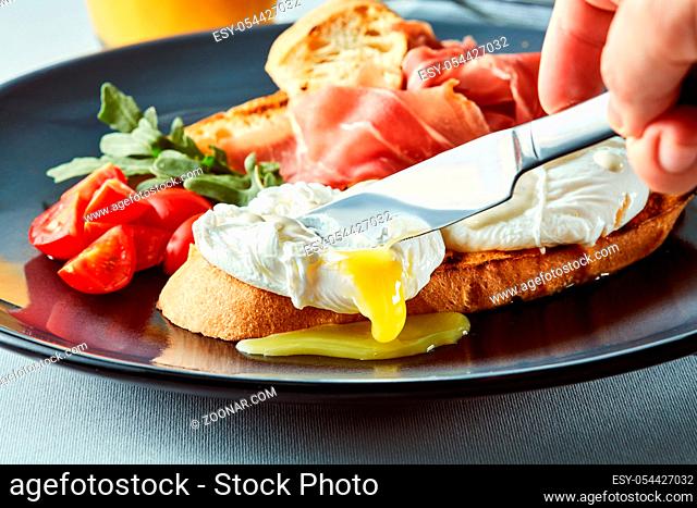 Healthy Breakfast with Wholemeal Bread Toast and Poached Egg. Man's hand with a knife cutting an egg