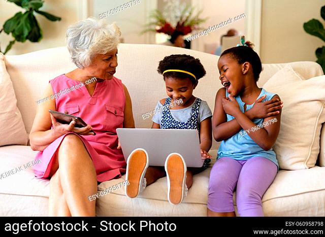 African american grandmother and her two granddaughters using laptop sitting on couch at home