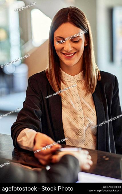 Smiling businesswoman paying contactless with smartphone at reception