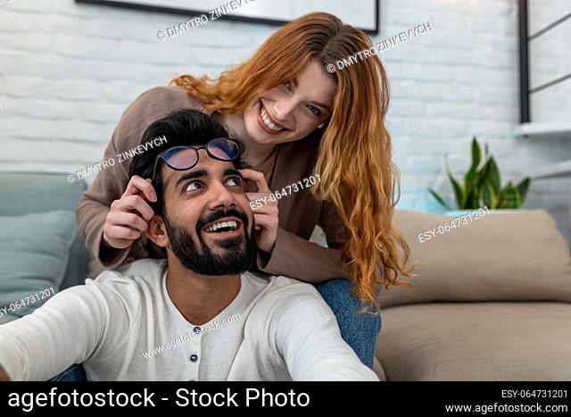 Happy married young couple sitting in room together, woman and man having fun, enjoying leisure time, relaxing at home, good relationship
