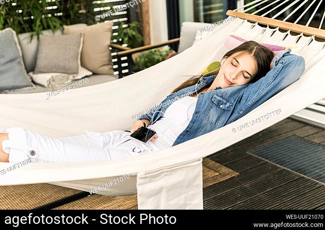 Beautiful woman listening music while relaxing on hammock in yard
