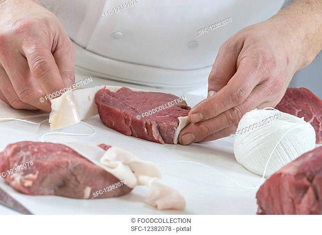 A chef wrapping a fillet steak in bacon