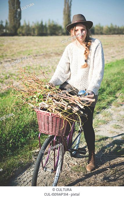 Young woman carrying bunch of sticks on bicycle