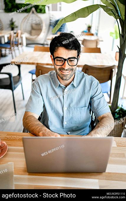 Smiling young businessman using laptop at table in cafe