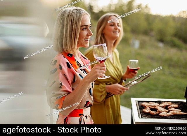 Female friends holding wine glasses and barbecuing meat