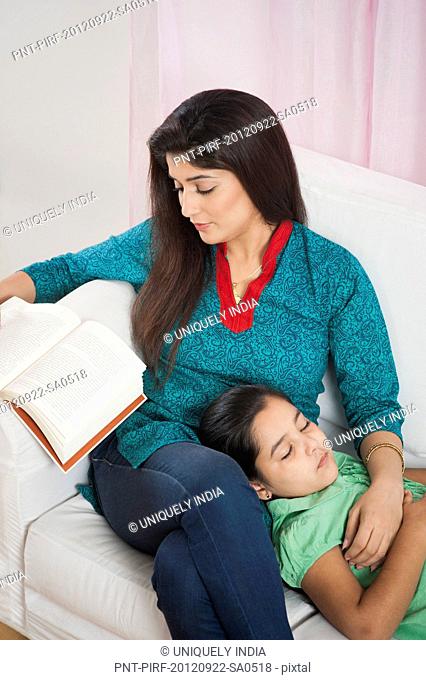 Woman reading a book with her daughter sleeping on her lap