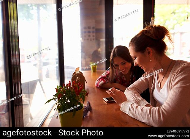 Toned picture of best friends ladies communicating in cafe or restaurant while sitting at table and looking at mobile or smart phone