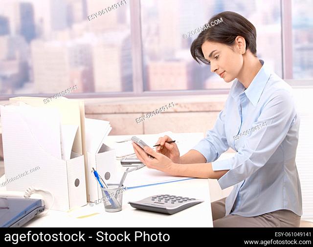 Smiling mid-adult woman working at office desk, using PDA