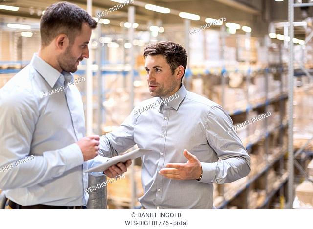 Two men with tablet talking in factory warehouse