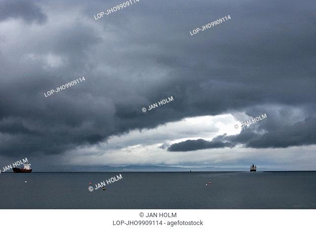 Scotland, North Ayrshire, Isle of Arran, Stormy skies over a cargo ship and The MV Caledonian Isles, a ferry that operates between Ardrossan on the Ayrshire...
