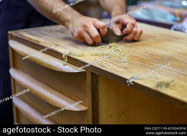 PRODUCTION - 10 July 2023, Saxony, Leipzig: Kris Sullivan removes old varnish from a sideboard ""Model 602k"" from Deutsche Werkstätten Hellerau