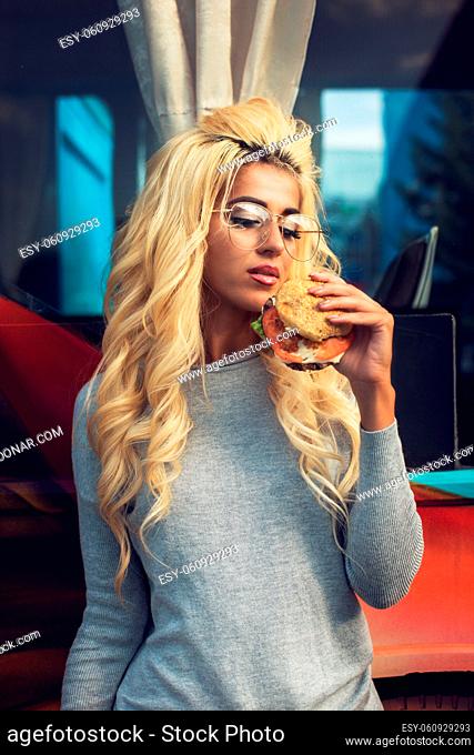 Fast street food concept - beauty young blonde woman eating a burger and soda water near the food truck