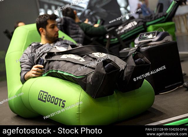 28 November 2023, Bavaria, Munich: Trade fair visitors try out a pair of multi-chamber regeneration pants at the Reboots stand during the ISPO sporting goods...