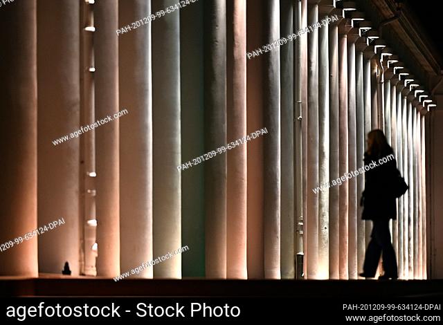 09 December 2020, Hessen, Wiesbaden: In the evening, a woman walks past the illuminated columns of the Kurhaus colonnades. Photo: Arne Dedert/dpa