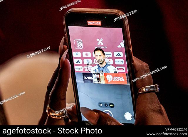 Belgium's head coach Domenico Tedesco is seen on the screen of a mobile phone held in her hands by a woman with very long fingernails and wearing several rings