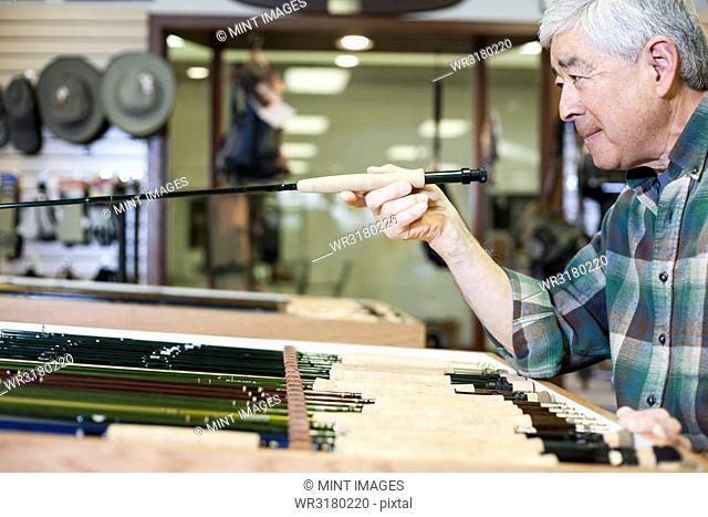Asian American senior male checking the balance on a 5 weight fly fishing rod for sale in a fly-fishing shop
