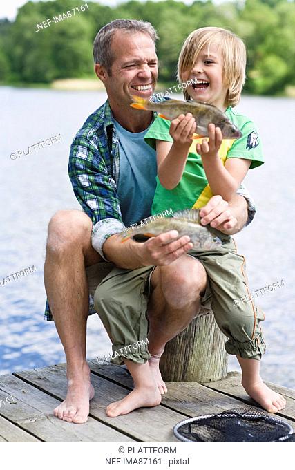 Father and son sitting on jetty, boy holding fish