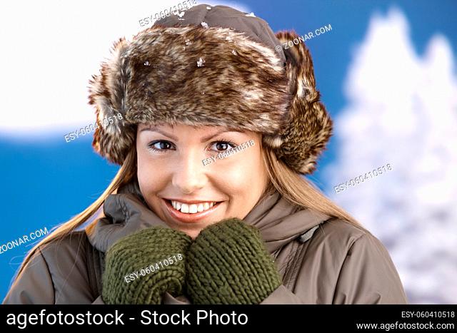Pretty young girl dressed up warm in coat, fur-hat and gloves, smiling, freezing