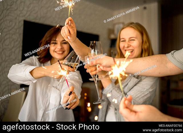 Cheerful friends celebrating with glasses of champagne and sparklers at home
