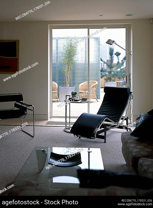 Modern sitting room with a carpeted floor, leather recliner, sofa, glass top coffee table, and a sliding glass door out to a rooftop patio