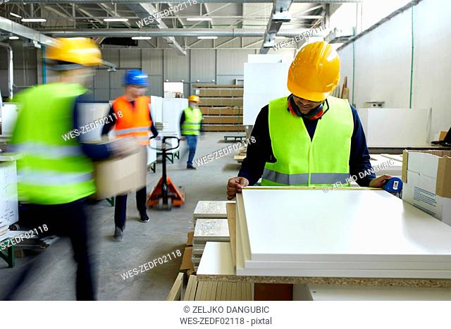 Worker examining wooden boards in factory with colleagues moving in background
