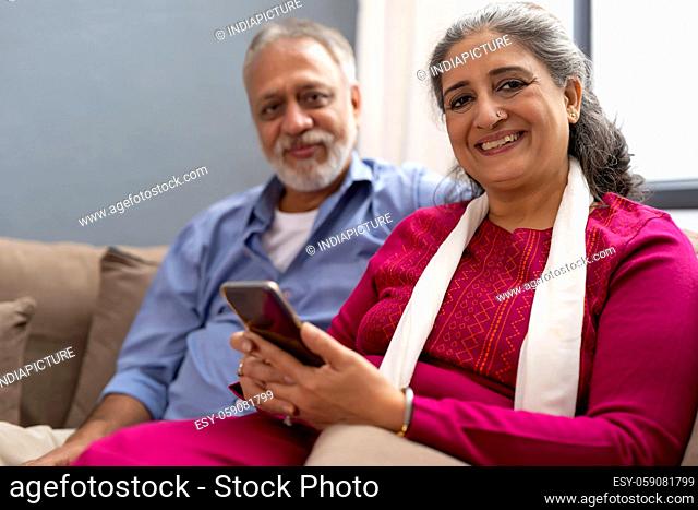 A SENIOR ADULT WOMAN SITTING WITH HUSBAND HOLDING MOBILE PHONE