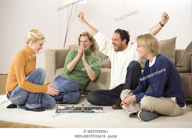 Family playing board game, man with arms outstretched, smiling