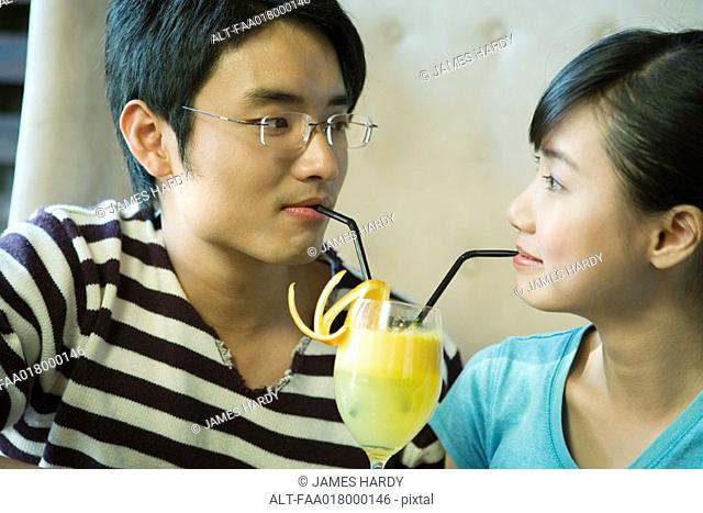 Young couple sharing cocktail with two straws