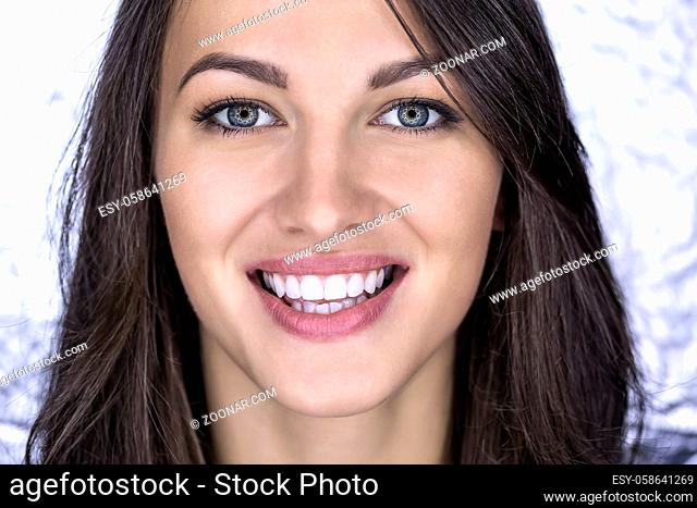 Beautiful girl with a broad smile looks into the camera on the blurry bright background. Close-up face portrait. Horizontal