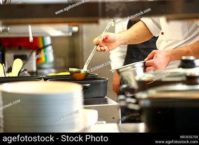 professional cook in kitchen preparing food for customers showing hands and a cook grabbing some yellow sauces