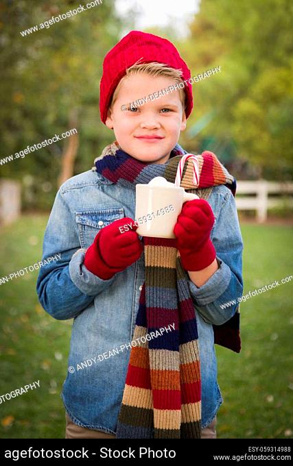 Handsome Young Boy Wearing Holiday Clothing Holding Hot Cocoa with Marshmallows and Candy Cane Outside