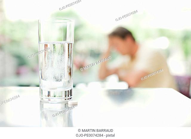 Glass of water and pill with unhappy man in background