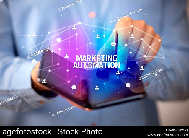 Businessman holding a foldable smartphone with MARKETING AUTOMATION inscription, new technology concept