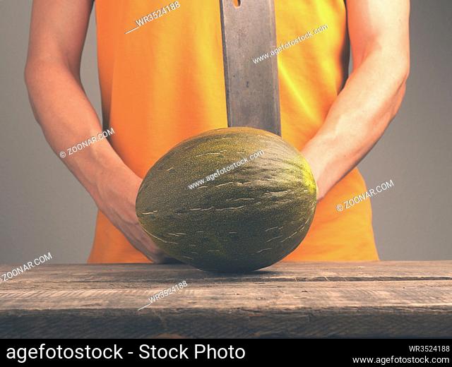 Young man with an old cleaver and a fresh melon on a rustic kitchen table