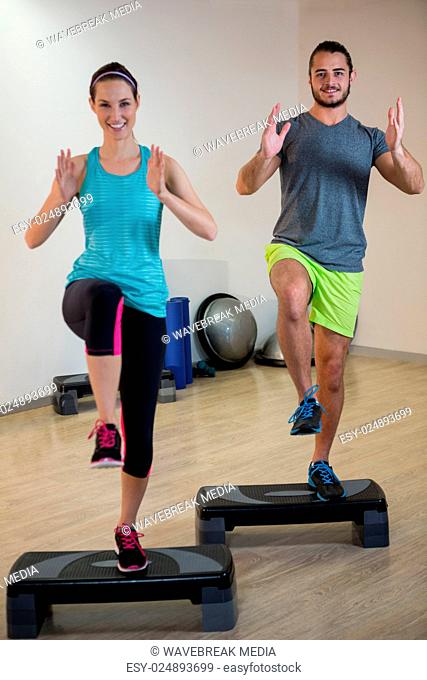 Smiling man and woman doing step aerobic exercise on stepper