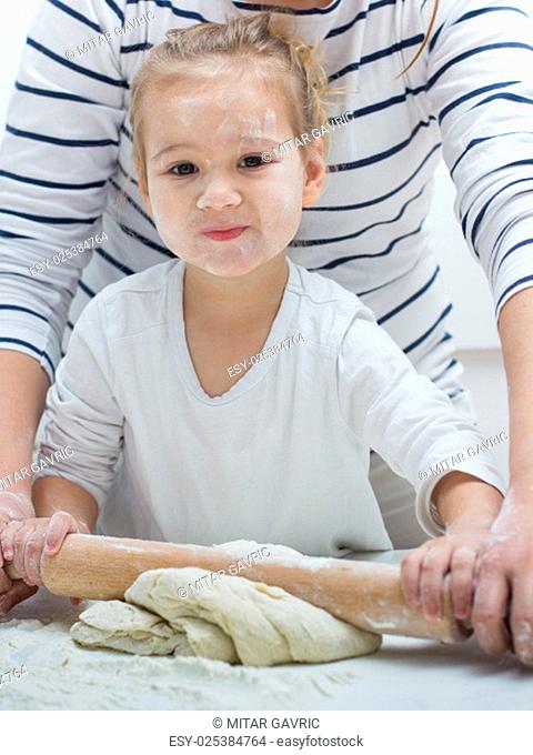 Cute little girl with her mother kneading dough at home