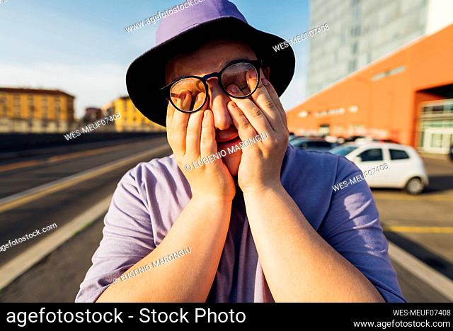 Teenage boy covering face with hands on sunny day