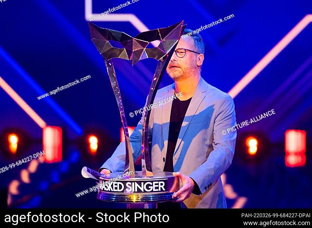 26 March 2022, North Rhine-Westphalia, Cologne: Matthias Opdenhövel stands on stage behind the winner's trophy in the Prosieben show ""The Masked Singer""