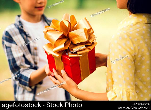 Boy giving little girl pretty gift. Cropped picture of little boy giving girl present in red wrapping paper with big golden ribbon bow