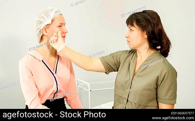 professional therapist in sterile gloves examines beauty clinic woman patient touching cheeks and lips