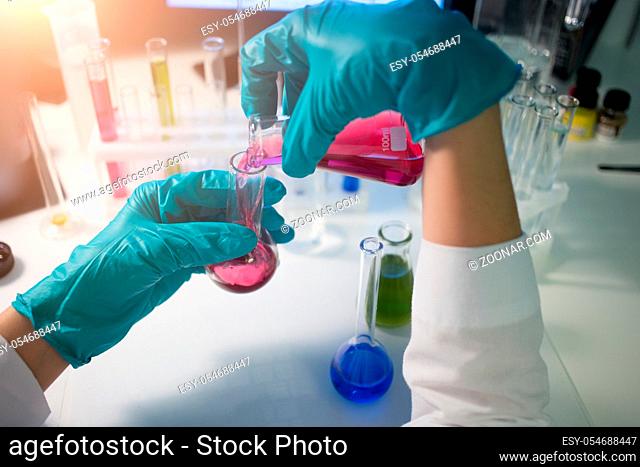 Lab assistant carries chemical testing with reagents in flasks at desk