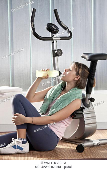 Woman drinking water by exercise machine