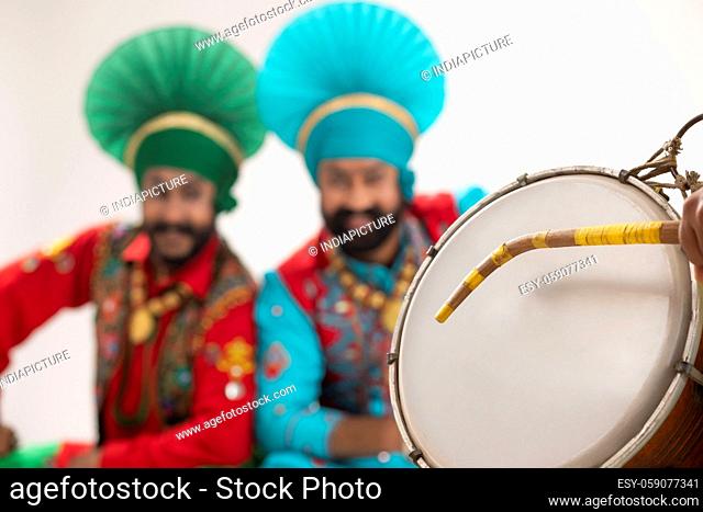 Two Bhangra dancer sitting as a blurred backdrop for a Dhol