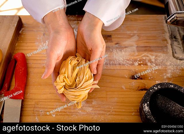 High angle close up view of the hands of a Caucasian female chef wearing chefs whites holding fresh pasta, dough rolled through a pasta machine