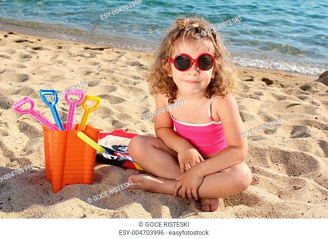 little girl with sunglasses sitting on beach